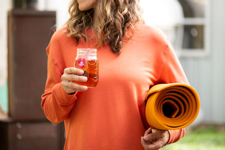 Women in orange sweater holding yoga mat drinking herbal cleanse tea