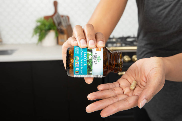 woman taking bacopa capsules in her kitchen
