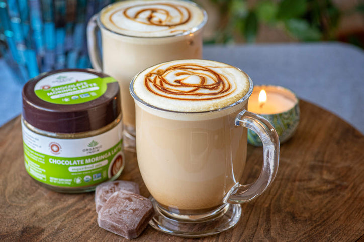Hot chocolate moringa latte with chocolate drizzle beside a candle on a wood table