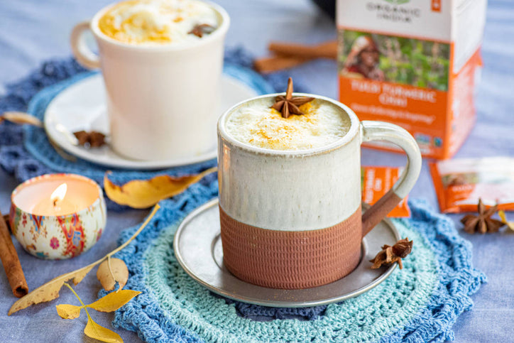 Golden chai latte in ceramic cup on handknitted blue placemat and autumn leaves.