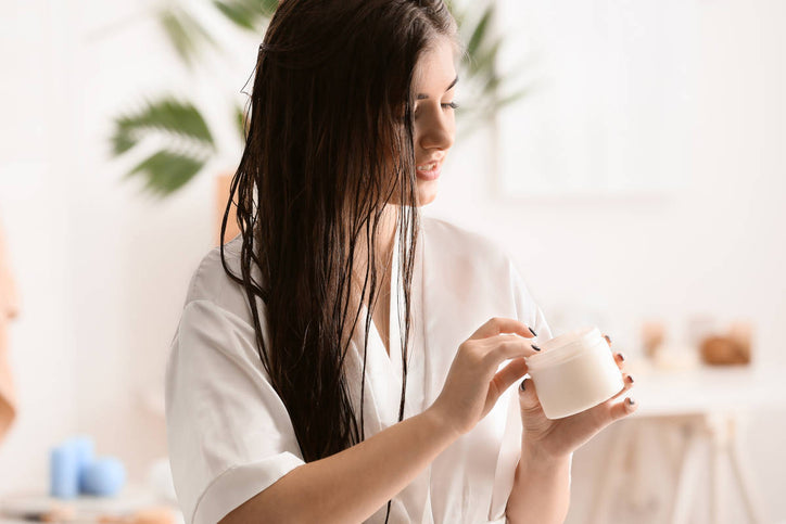 woman with long hair taking out cream from a jar