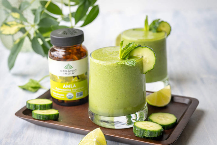 green cucumber smoothie on a tray with cucumber and lime garnish and amla capsules.