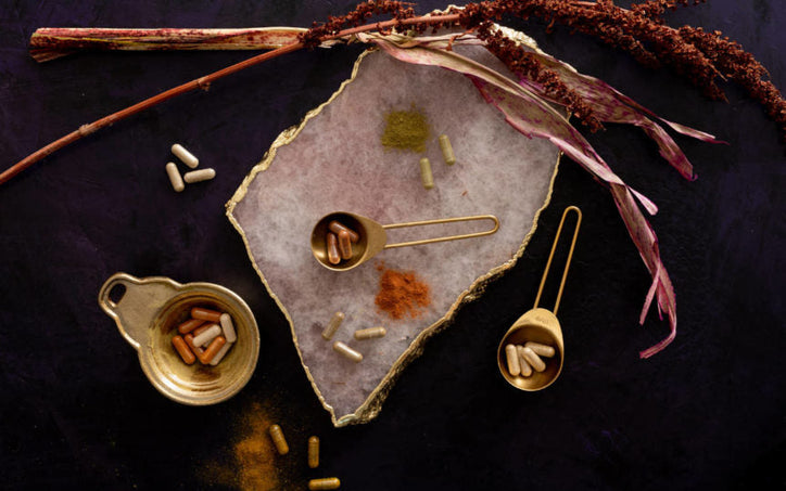 Various herbal capsules and powders on a black table and stone plank.