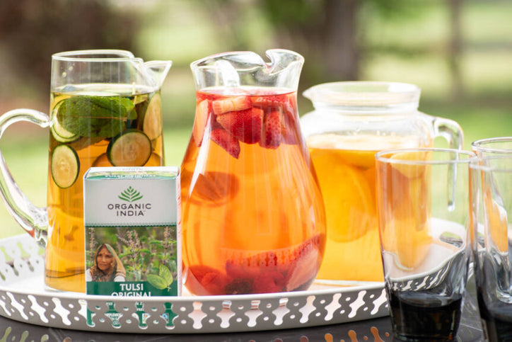 Tulsi cold brew (holy basil iced tea) in pitchers with different garnishes like strawberry, cucumber, mint and lemon.